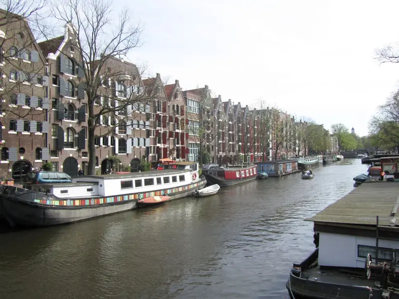 Canal Brouwersgracht com barcos-casa atracados e antigos armazéns de tijolo com janelas com venezianas na margem esquerda