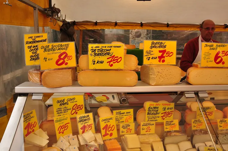 Banca de queijos holandeses com placas amarelas de preço escritas à mão na Albert Cuypmarkt