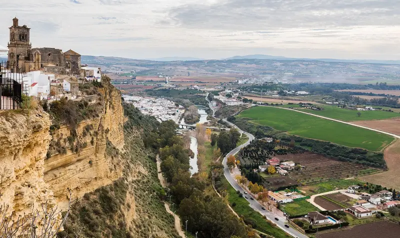 Arcos de la Frontera no alto de um paredão, com o rio e o campo verde lá embaixo
