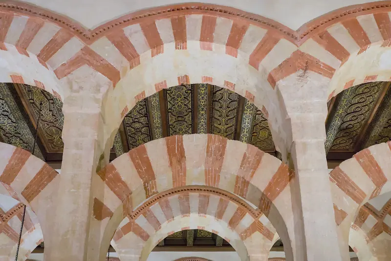 Arcos duplos listrados de pedra clara e tijolo vermelho sob o teto de madeira pintada da Mezquita de Córdoba