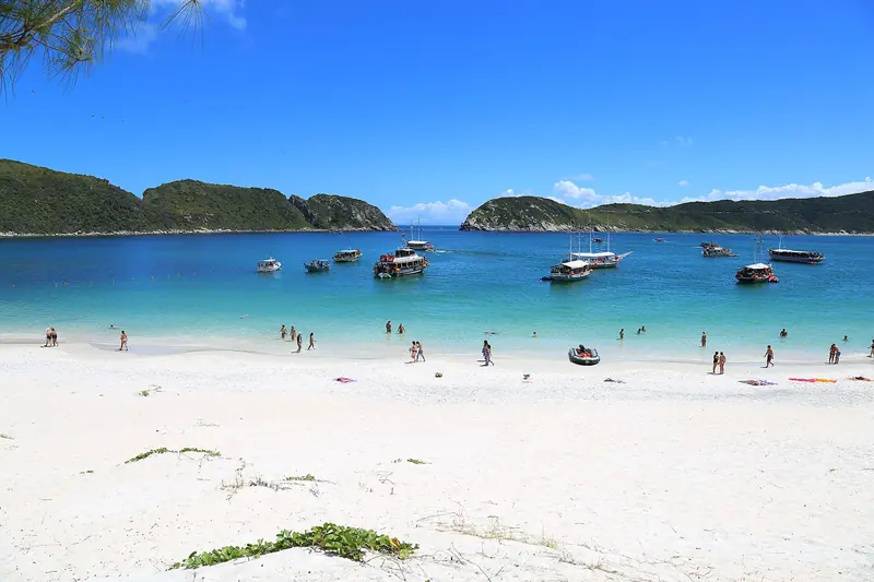Praia da Ilha do Farol com areia branca, barcos de passeio ancorados e a saída da ilha para o mar aberto ao fundo