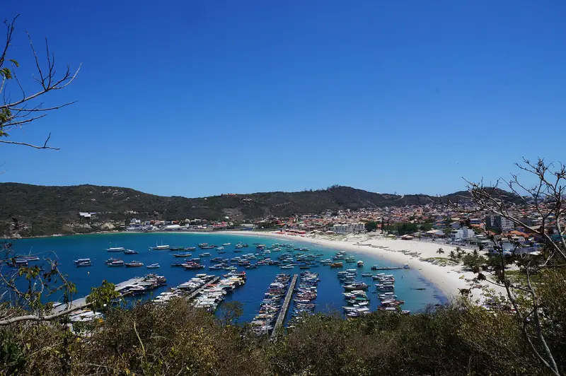 Praia dos Anjos vista do alto, com a marina cheia de barcos, a areia curva e as casas da cidade ao fundo