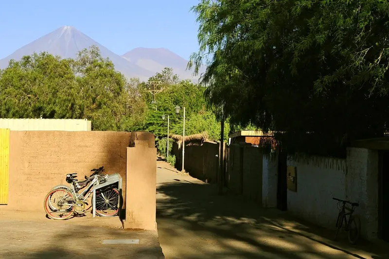 Rua de terra entre muros de adobe, com bicicletas encostadas e o vulcão Licancabur ao fundo