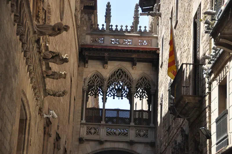 Ponte neogótica de pedra rendada sobre o Carrer del Bisbe, com bandeira catalã numa sacada