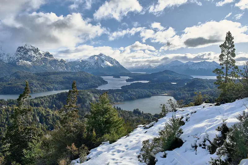 Do alto nevado do Cerro Campanario, braços de lago entre florestas e montanhas nevadas ao fundo