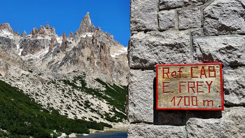 Placa de madeira do Refugio Frey, a 1.700 metros, na parede de pedra, com as agulhas de granito do Catedral ao fundo