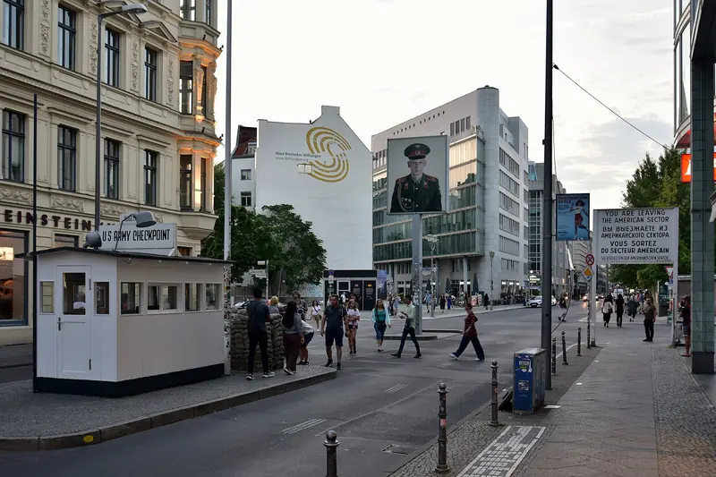 Réplica da guarita do Checkpoint Charlie com sacos de areia, a placa que avisa a saída do setor americano e o retrato de um soldado num poste no meio da Friedrichstraße