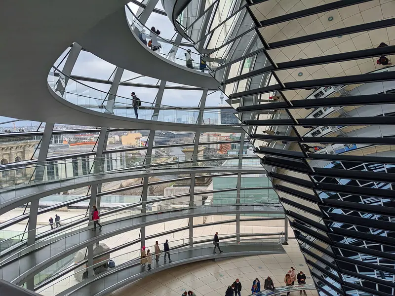Interior da cúpula do Reichstag, com visitantes subindo as rampas em espiral ao lado do cone central de espelhos e a cidade vista pelo vidro