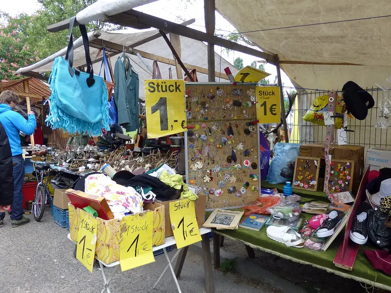 Barraca de feira de pulgas com bolsas, botons e sapatos, com placas amarelas de preço de 1 euro escritas à mão