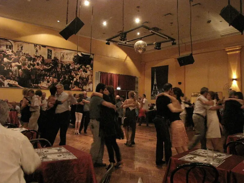 Casais dançando tango na pista de madeira do Salón Canning, entre mesas de toalha vermelha