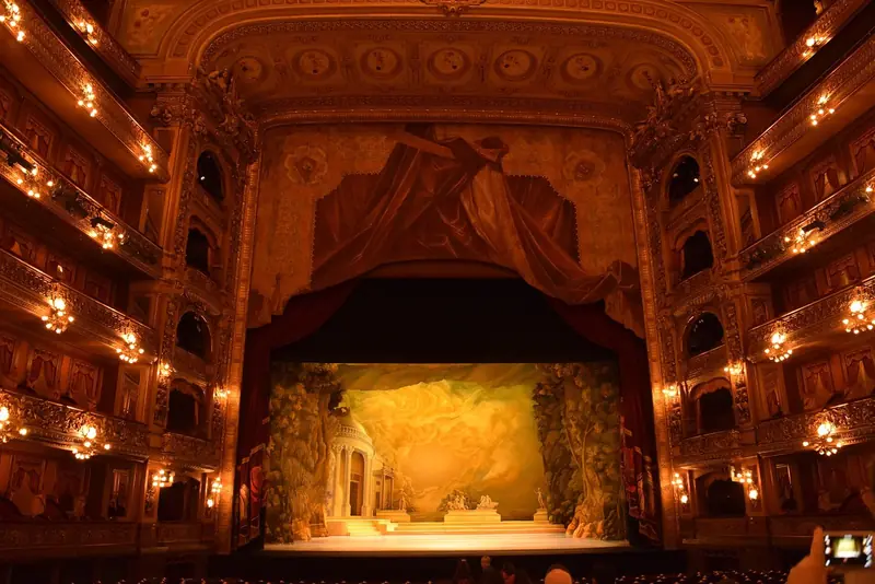 Sala principal do Teatro Colón, com camarotes dourados iluminados e o palco com cenário pintado