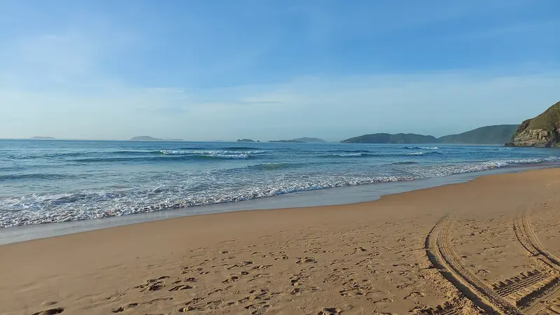 Faixa larga de areia de Geribá com ondas quebrando e morros ao fundo