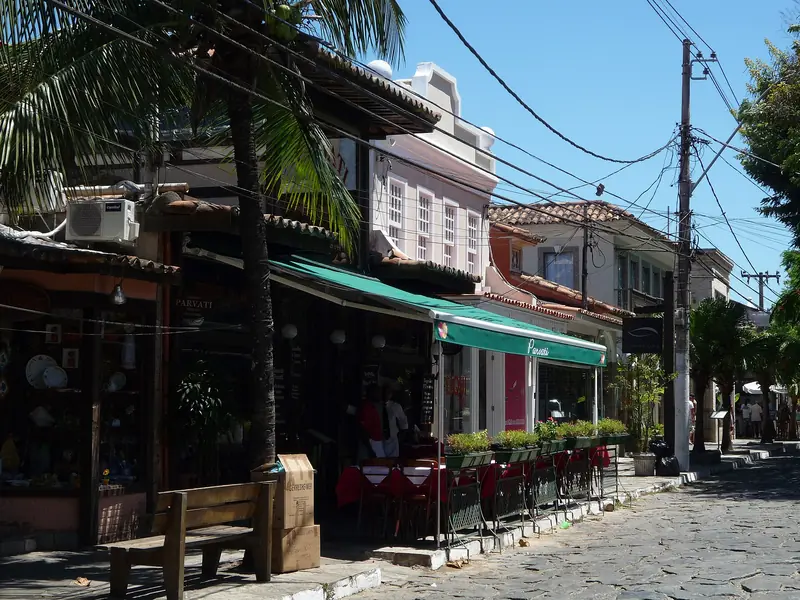 Rua das Pedras com restaurantes de toldo verde, mesas na calçada de pedra e palmeiras