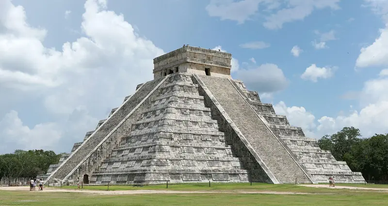 Pirâmide de Kukulcán, o Castillo de Chichén Itzá, com escadarias de pedra em duas faces sob céu azul com nuvens