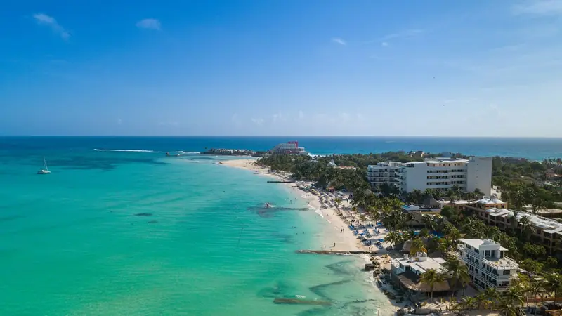 Vista aérea da Playa Norte, em Isla Mujeres, com água verde-clara rasa, faixa de areia branca e coqueiros ao longo da orla