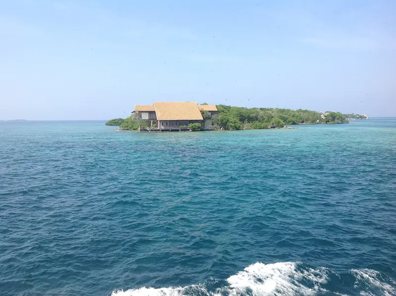 Ilhota com uma casa de telhado claro entre a vegetação, cercada de mar azul-turquesa nas Ilhas do Rosário