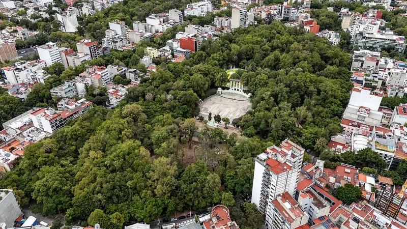 Vista aérea do Parque México, com copas de árvores em volta de uma concha acústica branca, cercado por prédios residenciais