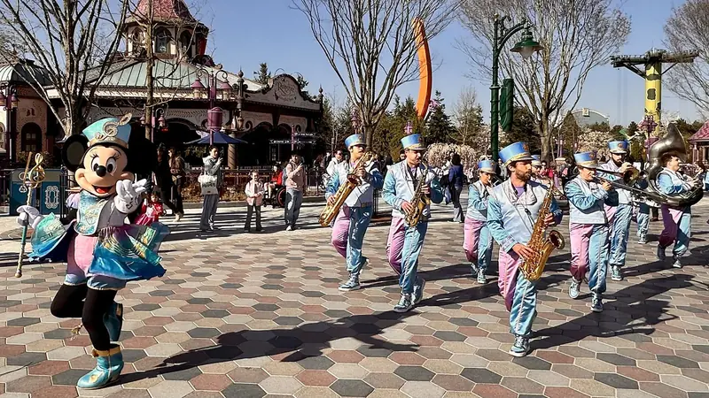 Banda da Disney marchando com Minnie na Adventure Way, com prédios novos e brinquedos ao fundo