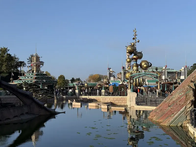 Lagoa de Discoveryland no fim da tarde, com o submarino do Nautilus, a torre do Orbitron e prédios metálicos refletidos na água
