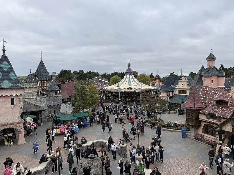 Rua central de Fantasyland com carrossel, casas de telhado pontudo e visitantes