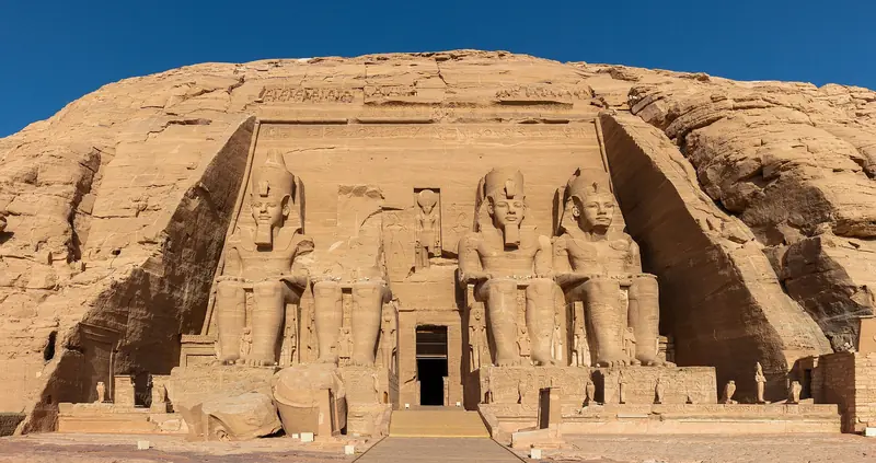 Fachada do grande templo de Abu Simbel escavada na rocha, com quatro estátuas sentadas de Ramsés II, uma delas sem cabeça, sob céu azul