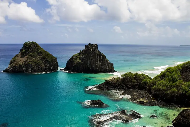 Os dois morros do Dois Irmãos saindo do mar azul-turquesa da Baía dos Porcos, vistos do alto