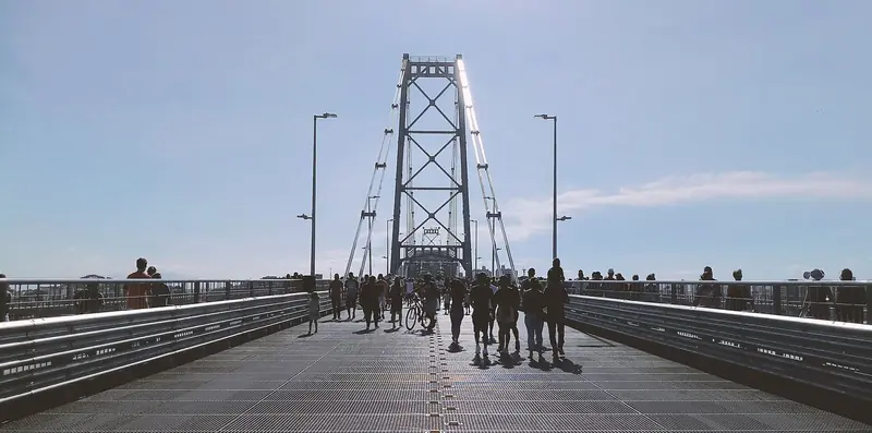 Pedestres na pista da Ponte Hercílio Luz, com a torre insular e os cabos de suspensão à frente