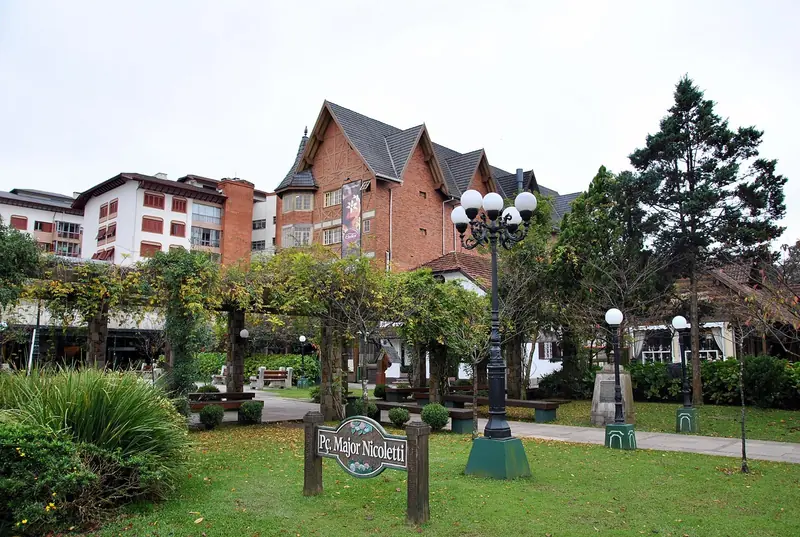 Praça Major Nicoletti com gramado, postes antigos e prédios de telhado pontudo ao fundo