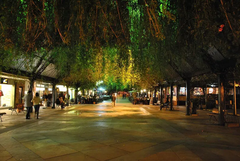 Calçadão da Rua Coberta à noite, com plantas penduradas no teto e mesas dos restaurantes