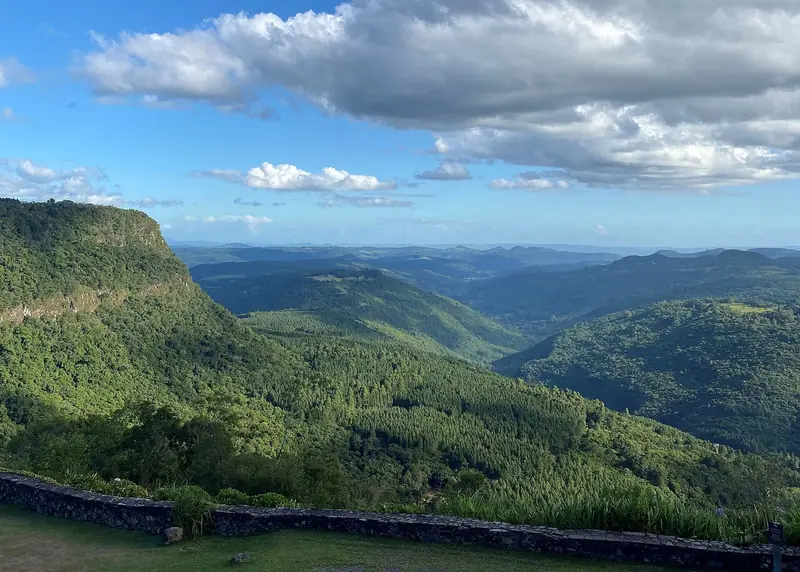 Vista do alto do Vale do Quilombo, com morros cobertos de mata e um muro de pedra em primeiro plano
