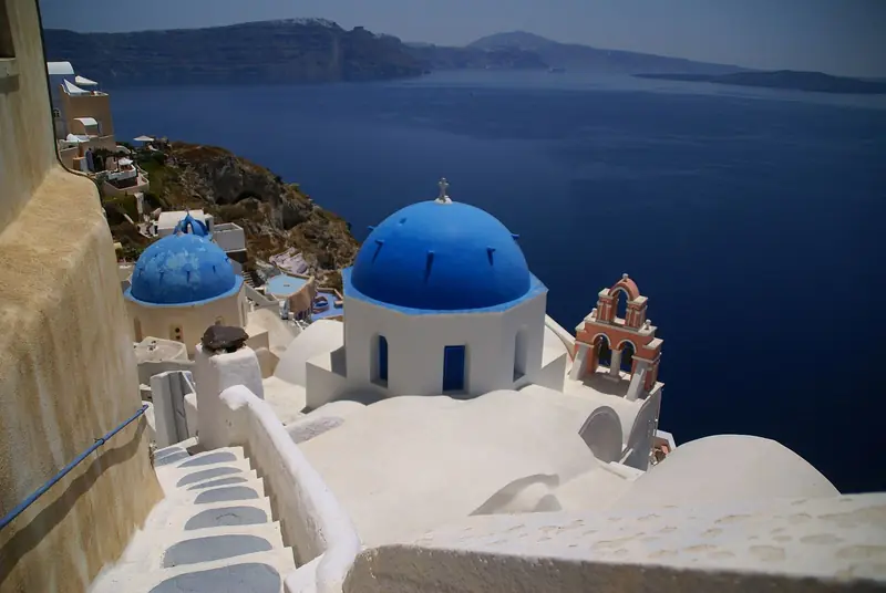 Igrejas de cúpula azul e campanário rosa em Oia, com a caldeira ao fundo