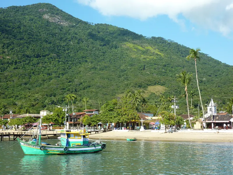 Barco de pesca verde ancorado diante da praia do Abraão, com o casario, a igreja branca e o morro coberto de mata ao fundo