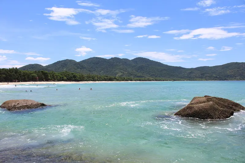 Água verde-azulada e pedras no canto da Praia de Lopes Mendes, com a faixa de areia e o morro ao fundo