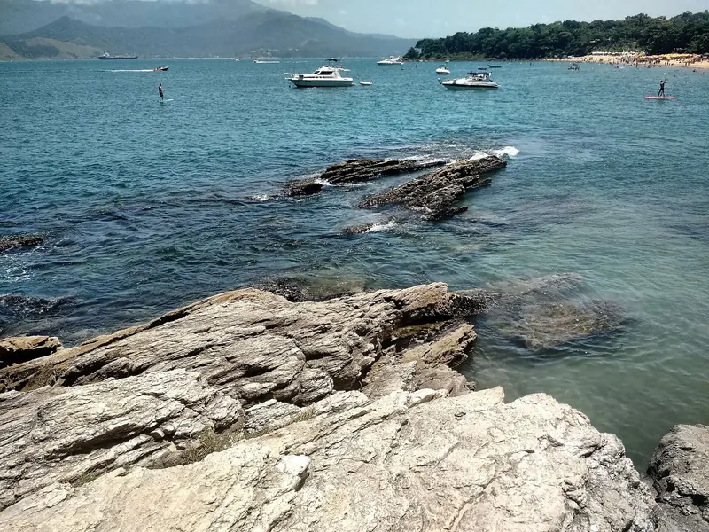 Costão e mar calmo na Praia do Curral, com barcos e a faixa de areia ao fundo