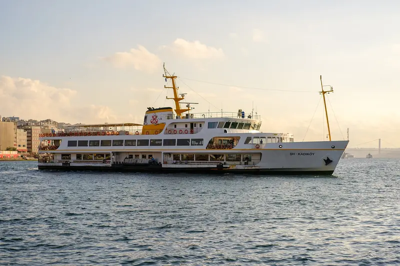 Ferry branco e amarelo da Şehir Hatları navegando no Bósforo, com a ponte suspensa ao fundo