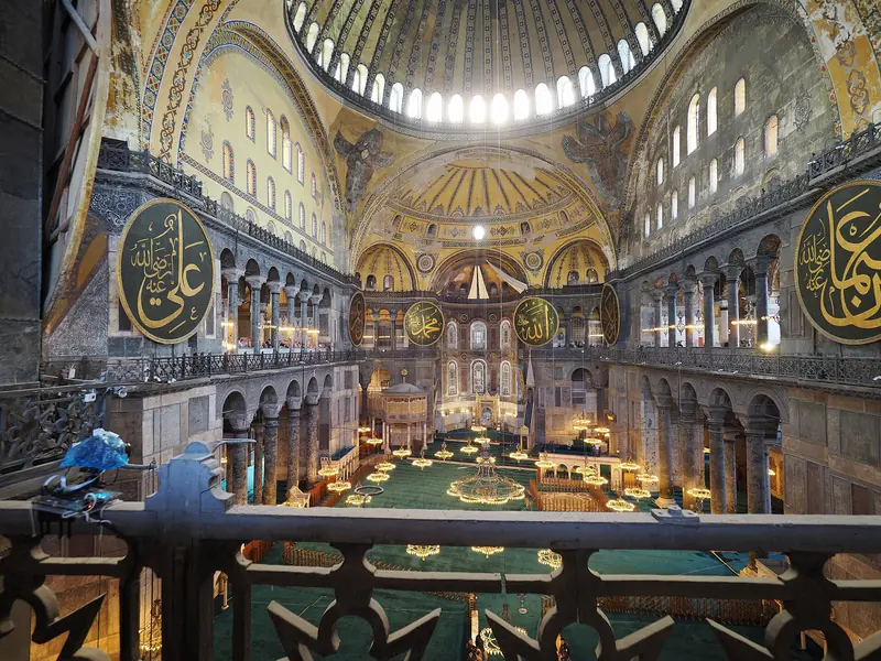 Interior da Hagia Sophia visto da galeria superior, com a cúpula, os medalhões de caligrafia e o tapete verde do piso térreo