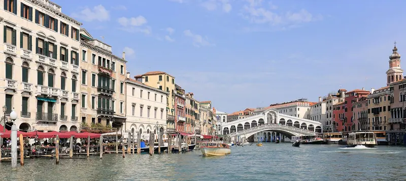 Grande Canal de Veneza com a Ponte de Rialto ao fundo, palácios coloridos nas margens e barcos atracados