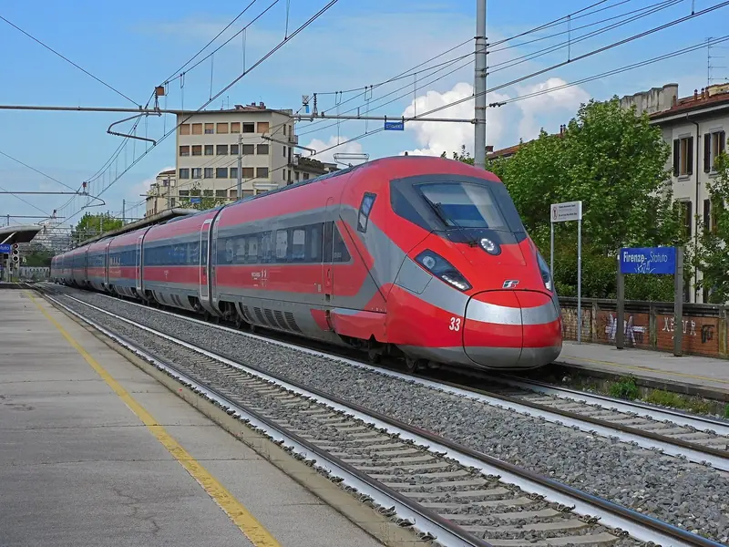 Trem Frecciarossa 1000 vermelho passando pela estação Firenze Statuto, em Florença, num dia de céu azul