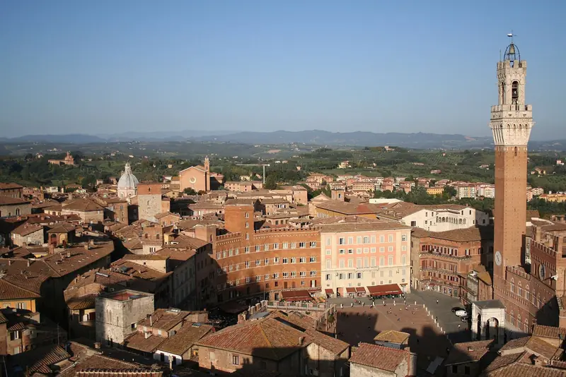 Piazza del Campo de Siena vista do alto, com a Torre del Mangia de tijolo à direita e os telhados e colinas da Toscana ao fundo