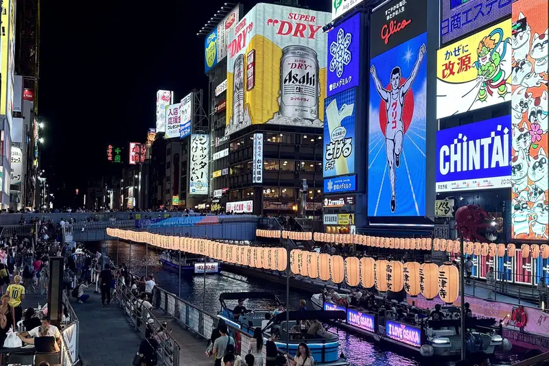 Canal de Dotonbori à noite, com painéis de neon enormes nos prédios, lanternas de papel e barcos de passeio na água