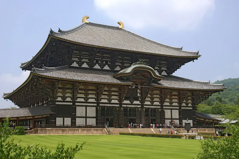 Grande salão de madeira do Todaiji, com telhado duplo e enfeites dourados no alto, atrás de um gramado