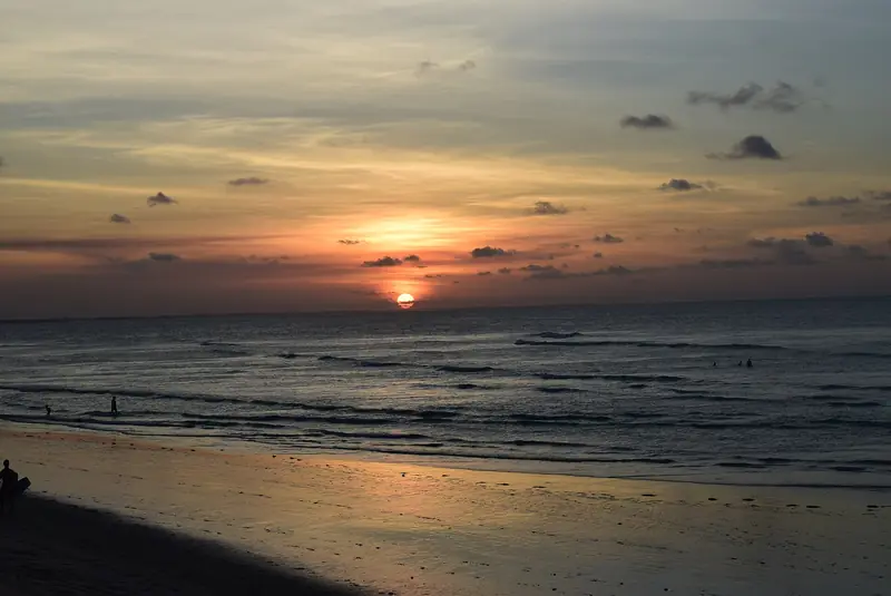 Sol baixo sobre o mar visto da praia de Jericoacoara, com a areia molhada refletindo a luz alaranjada