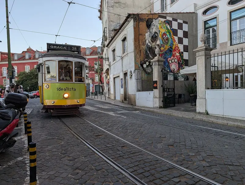 Elétrico amarelo da linha 28, com destino à Graça, numa rua de paralelepípedos