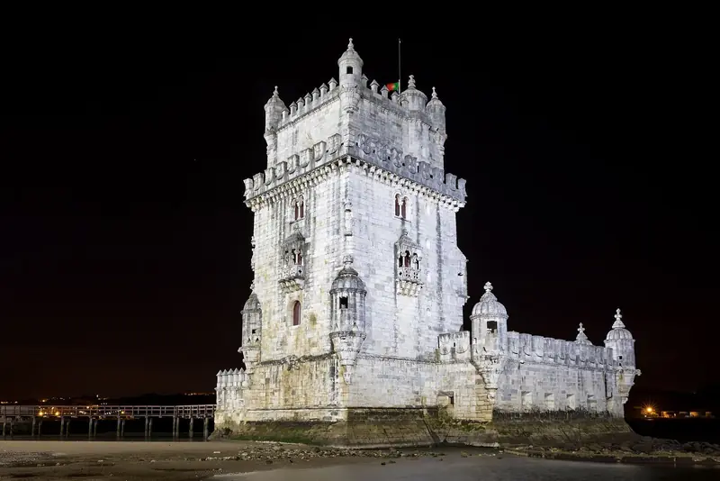 Torre de Belém iluminada à noite, sobre as pedras da margem do Tejo