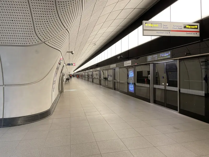 Plataforma longa da Elizabeth line na estação Tottenham Court Road, com teto curvo, portas de vidro ao longo da linha e placas de saída