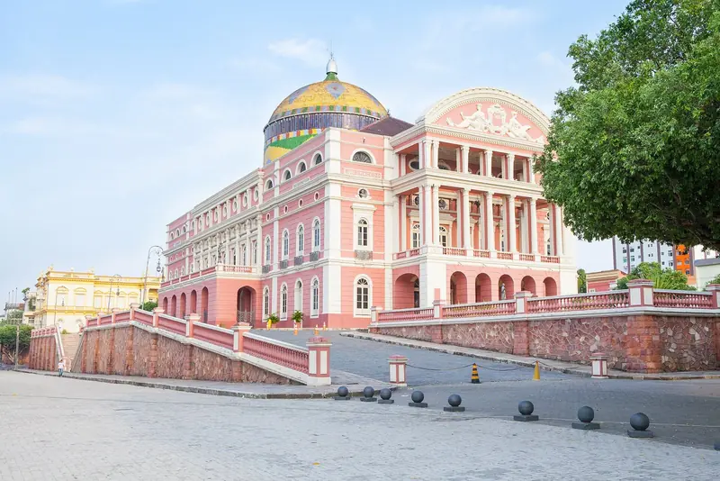 Fachada rosa e lateral do Teatro Amazonas com a cúpula colorida, vistas da rua ao lado