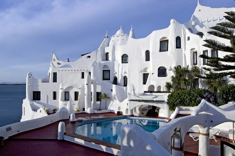 Casapueblo, em Punta Ballena: construção branca de paredes curvas e janelas pequenas sobre a encosta, com piscina e terraço vermelho à frente e o mar à esquerda