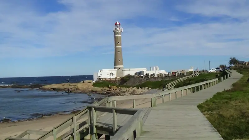 Farol de José Ignacio sobre a ponta de pedras, com uma passarela de madeira à beira-mar e o oceano ao fundo