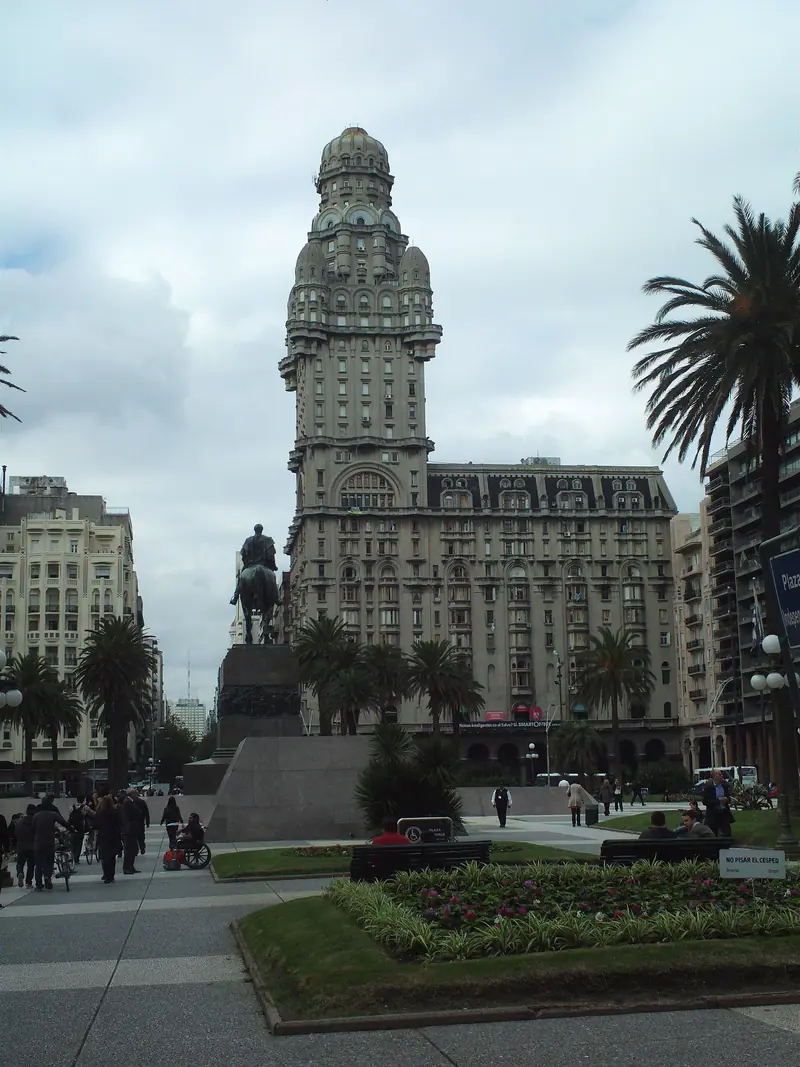 Palacio Salvo com sua torre ornamentada atrás da estátua equestre de Artigas, na Plaza Independencia, com palmeiras e canteiros