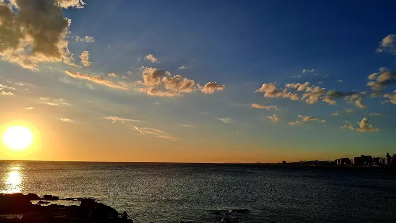 Pôr do sol sobre o Rio da Prata visto das pedras da Rambla de Punta Carretas, com a silhueta da cidade ao fundo